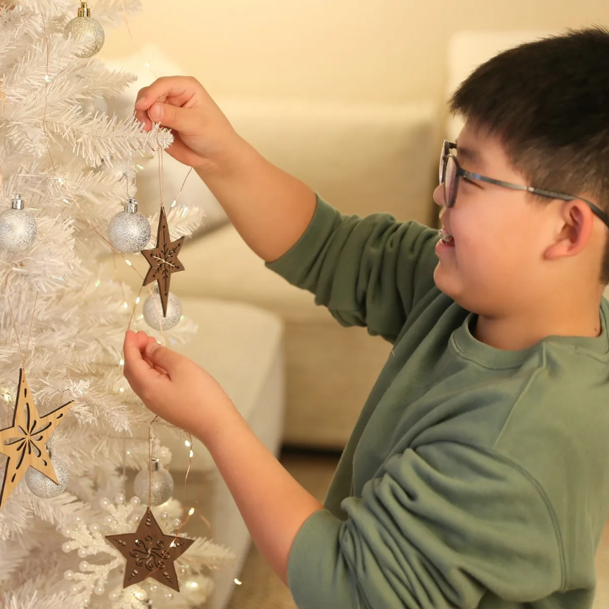 子どもが白いクリスマスツリーにウォールナットとくり材の天然木スターオーナメントを飾り付けている様子