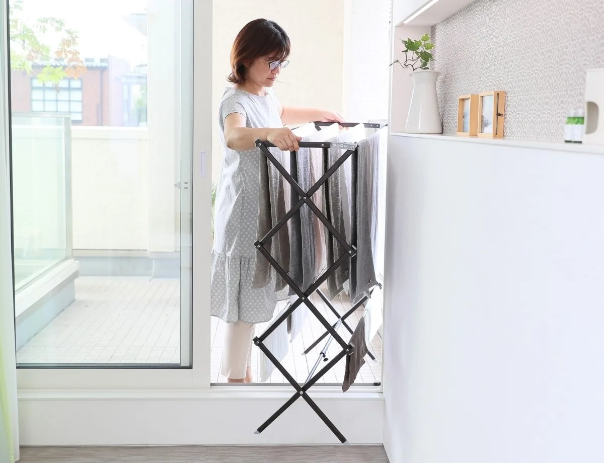 洗濯物を干したまま物干しスタンドをベランダへ移動する女性