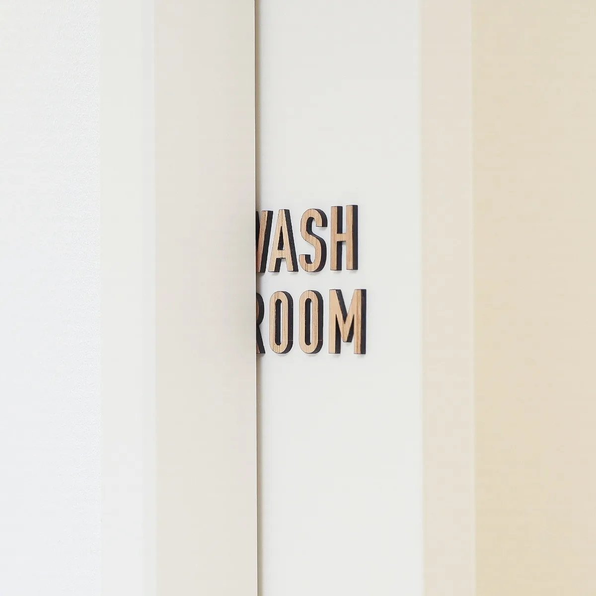 引き戸に貼られた天然木の「WASH ROOM」ドアサインプレート。引き戸対応の薄型デザイン