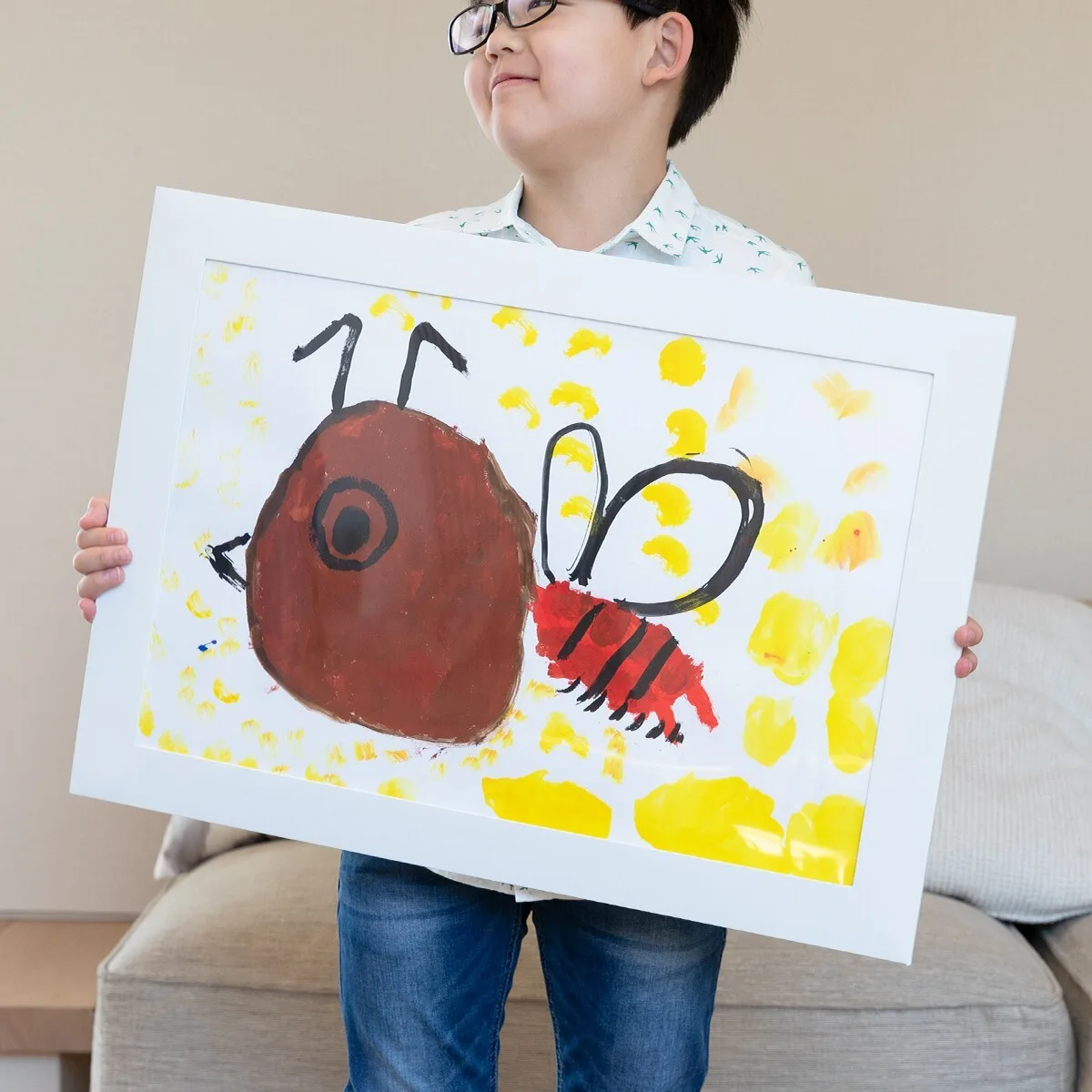 子どもの絵をペーパーフレームに入れて持つ眼鏡の男の子