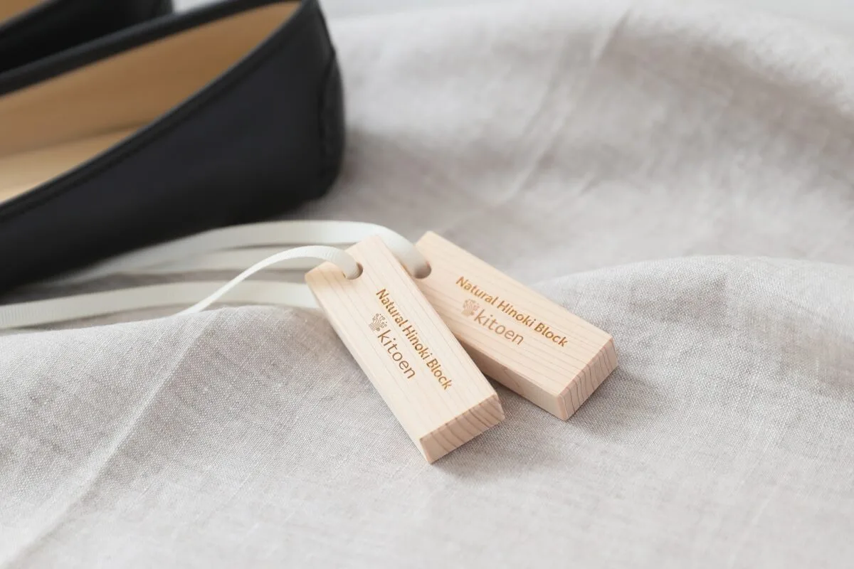 リネン布地の上に置いたkitoen Natural Hinoki Block 2個と黒い靴のクローズアップ