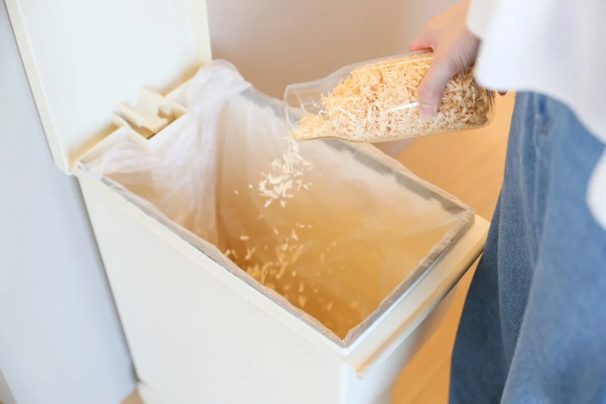 開いたペダル式ゴミ箱にガラス瓶からヒノキのかんなくずをそのまま注ぎ入れる使用シーン