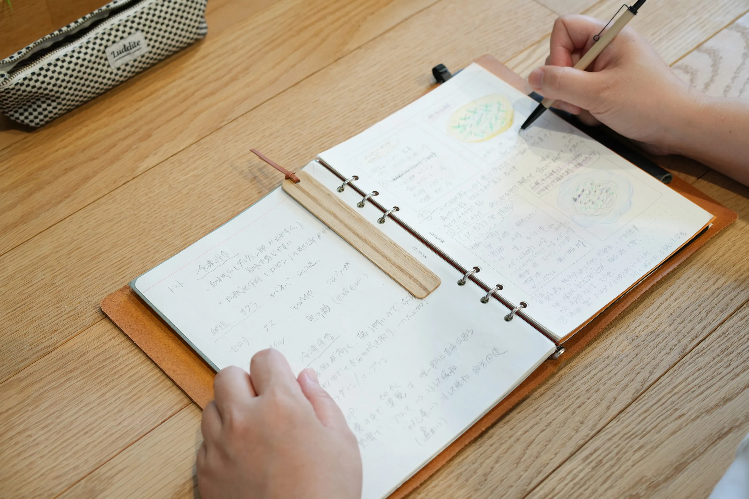 子どもが木製しおりを挟んだノートに読書感想文を手書きしている場面