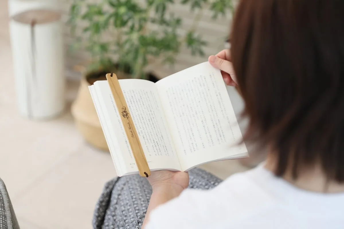 女性が本を読みながら名前・ドラム刻印の木製バンドしおりを使用している様子