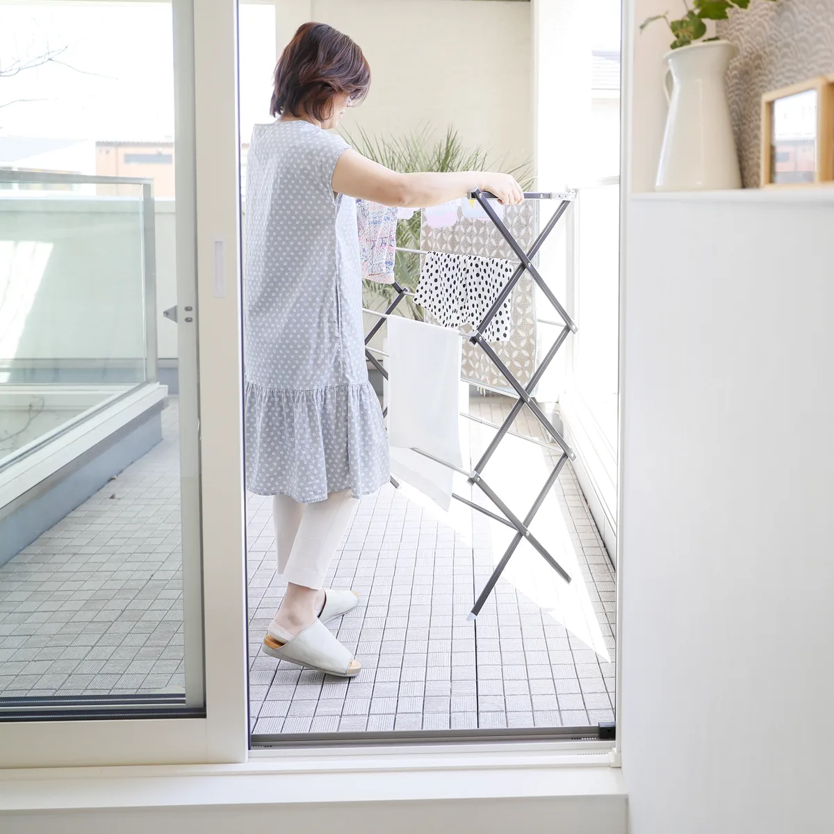 女性がベランダで折りたたみ式物干しスタンドに洗濯物を干している様子