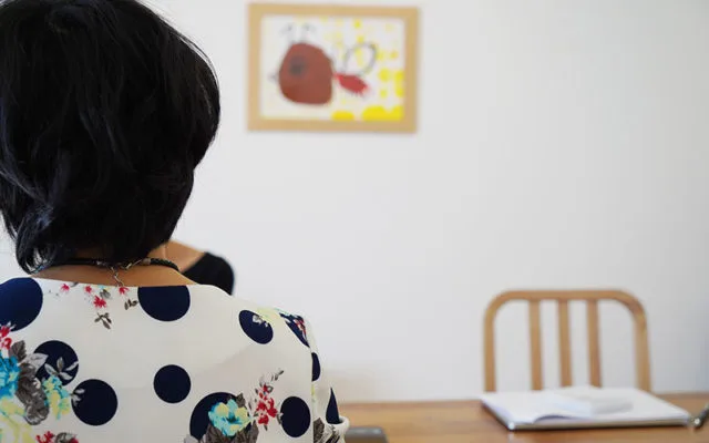 後ろ姿の女性が壁に飾られた子供のお絵かき作品をじっくり眺めている