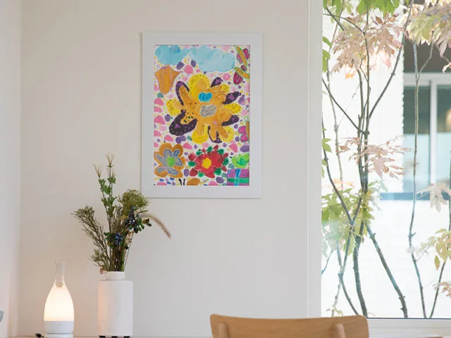 子供が描いた色鮮やかな花の絵を白いフレームに入れてリビングの壁に飾った様子