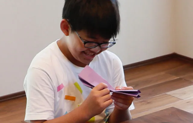 眼鏡をかけた男の子が笑顔で折り紙を折っている様子