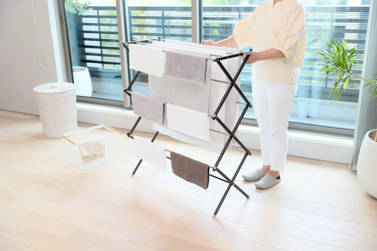 室内でWYのX型折りたたみ物干しスタンドにタオルを干す女性